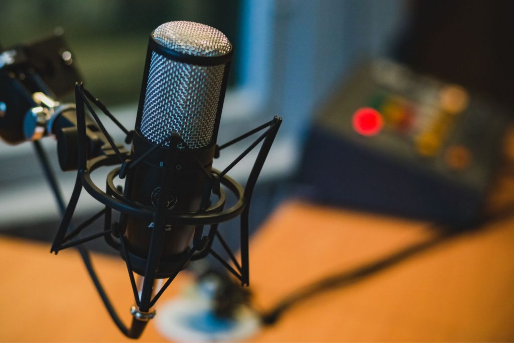 Podcast marketing: image shows a microphone in focus, with a table and podcast recording equipment blurred in the background.